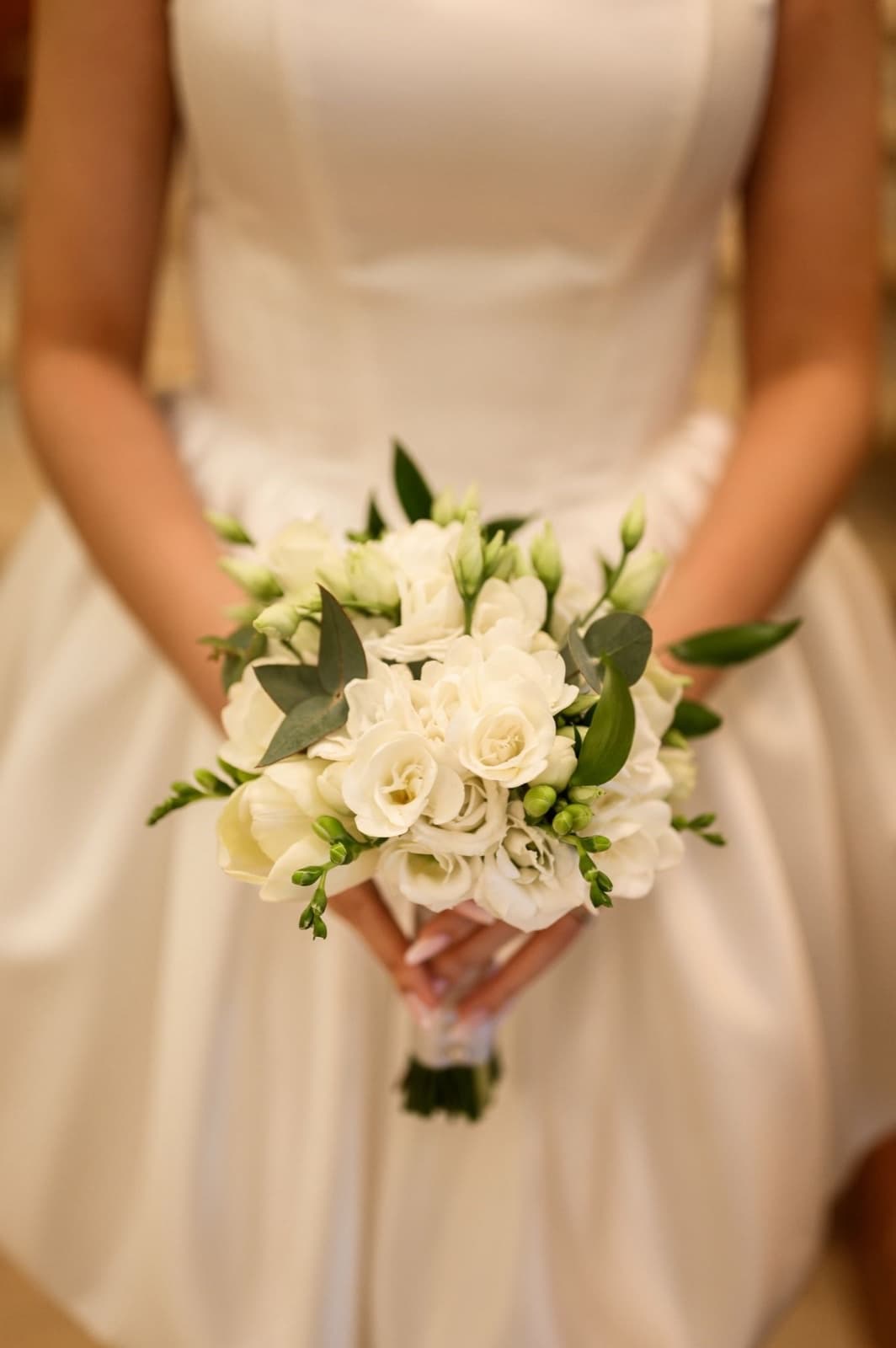 Mireasă ținând un buchet alb cu trandafiri, lisianthus și eucalipt